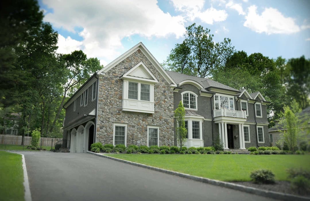 Elegant stone and gray siding house with a manicured lawn and spacious driveway.
