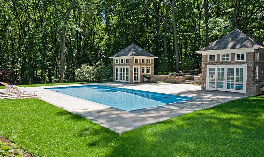 Elegant backyard pool surrounded by lush greenery and charming pool houses.