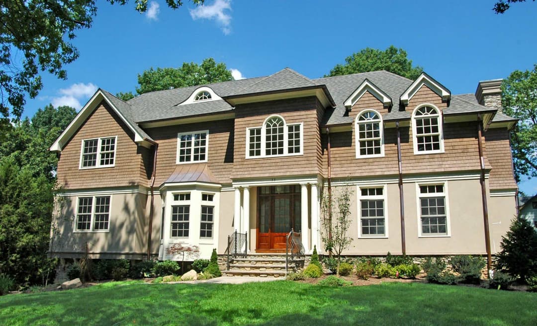 Elegant two-story house with a landscaped yard and large windows under a blue sky.