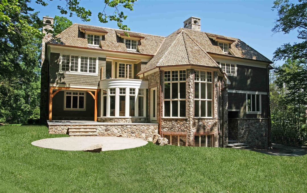 Elegant stone and wood house with large windows, surrounded by a lush green lawn.