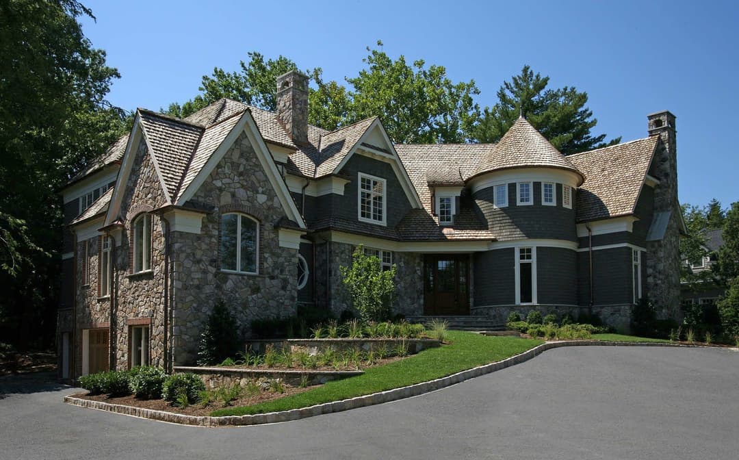 Elegant stone house with a unique design, featuring multiple gables and lush landscaping.