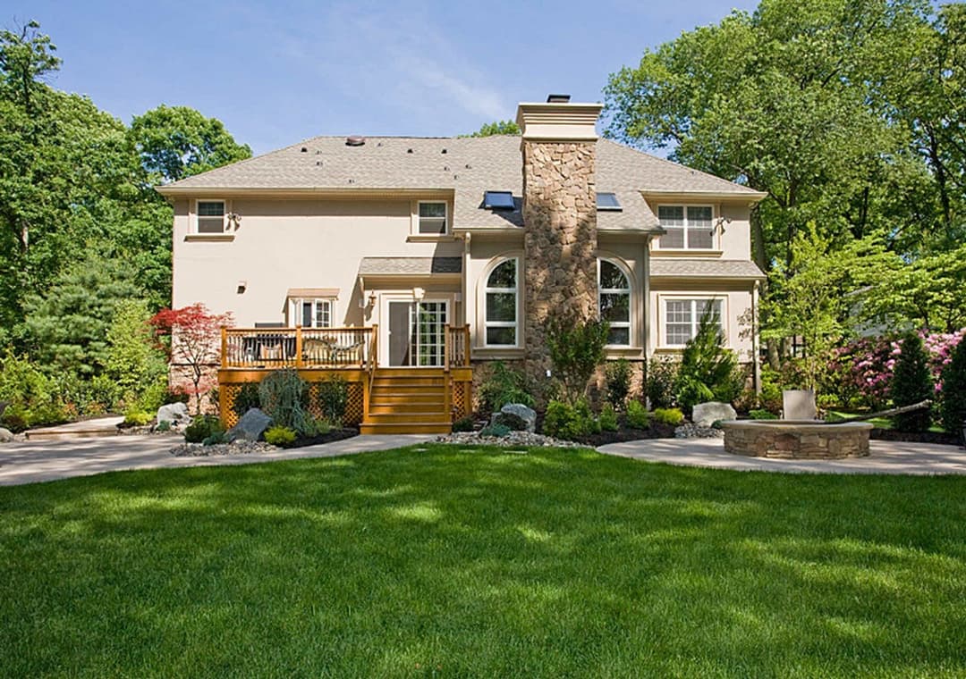 Elegant two-story home with a stone facade, surrounded by landscaped gardens and a patio.