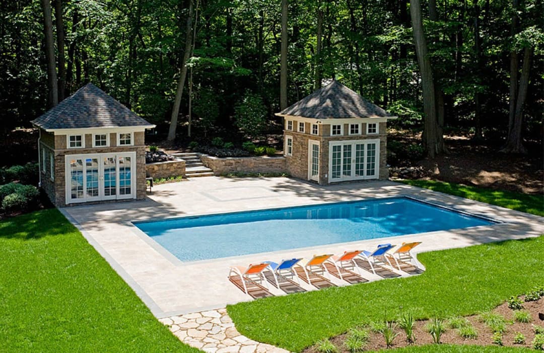 Elegant backyard with a pool, two cabanas, and colorful lounge chairs surrounded by greenery.