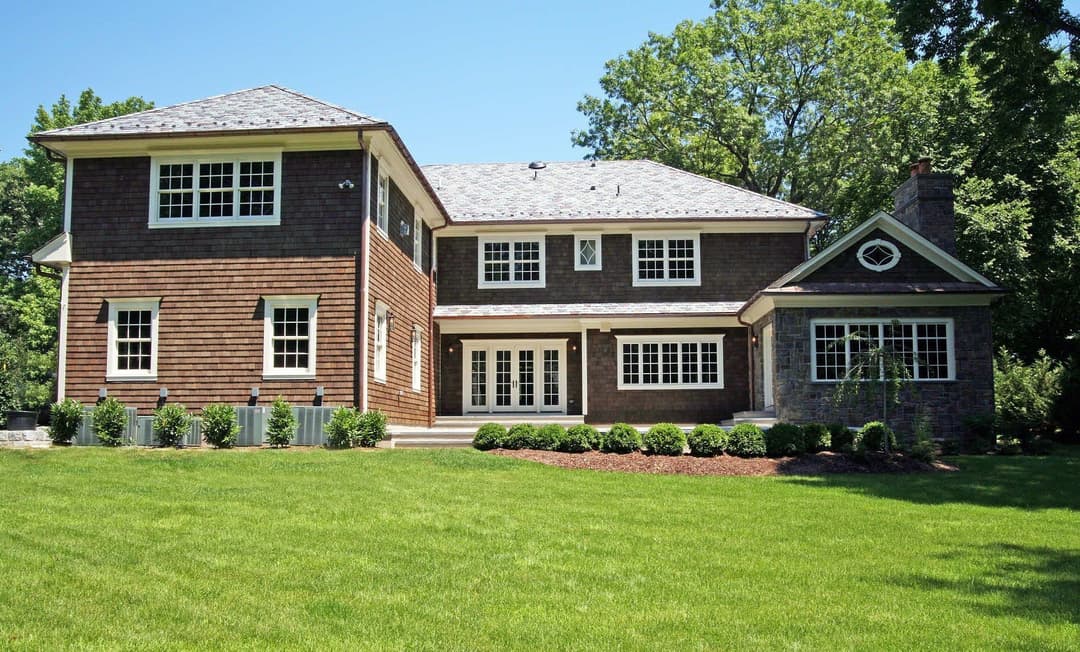 Modern two-story house with a landscaped yard and large windows on a sunny day.