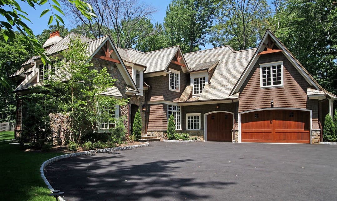 Luxurious brown house with stone accents and a spacious driveway, surrounded by trees.