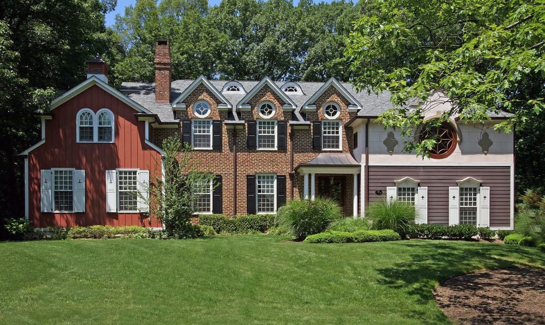 Elegant two-story brick and wood house with a landscaped lawn and trees.