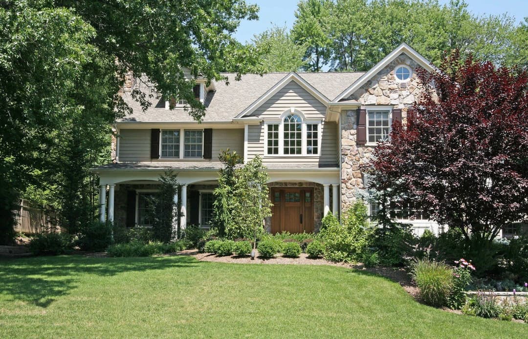 Beautiful residential home with stone accents, lush landscaping, and green grass in the front yard.