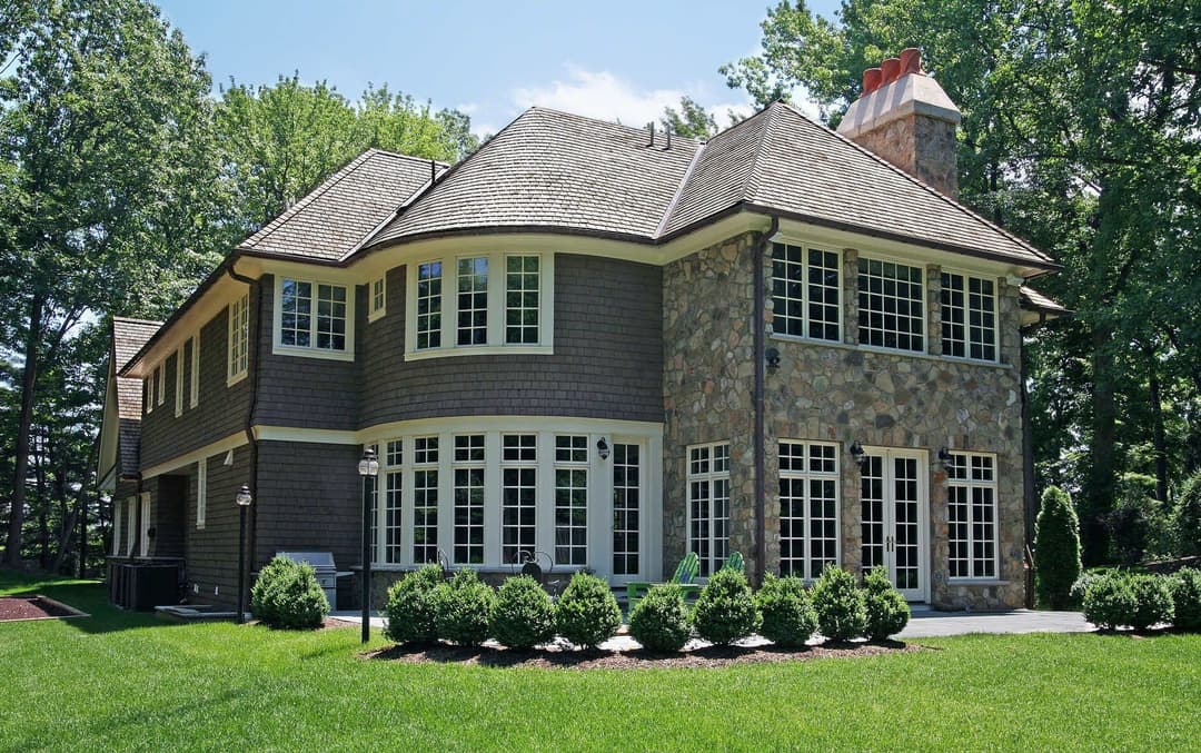 Elegant stone and wood exterior of a modern home with large windows and manicured landscaping.