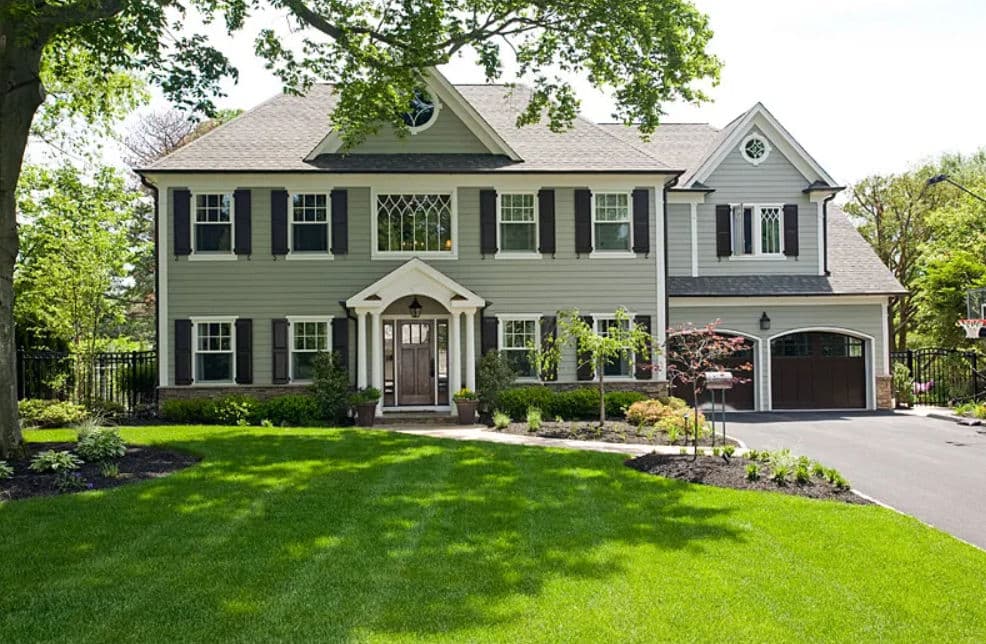 Beautiful gray colonial-style house with landscaped lawn and two-car garage.