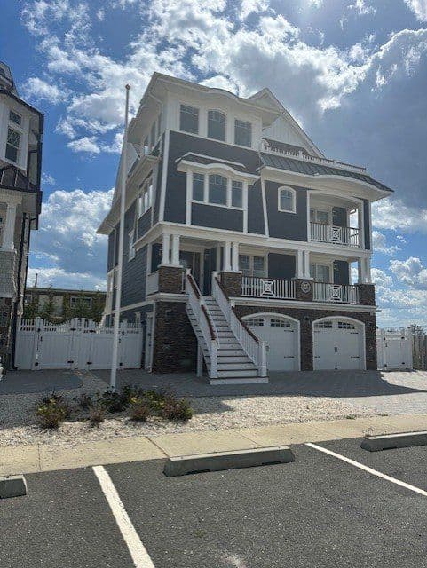 Modern coastal home with gray siding, stone accents, and white trim under a blue sky.
