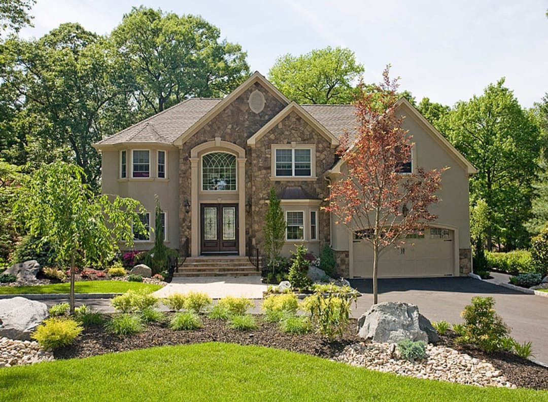 Elegant suburban home with stone accents, lush landscaping, and a manicured lawn.