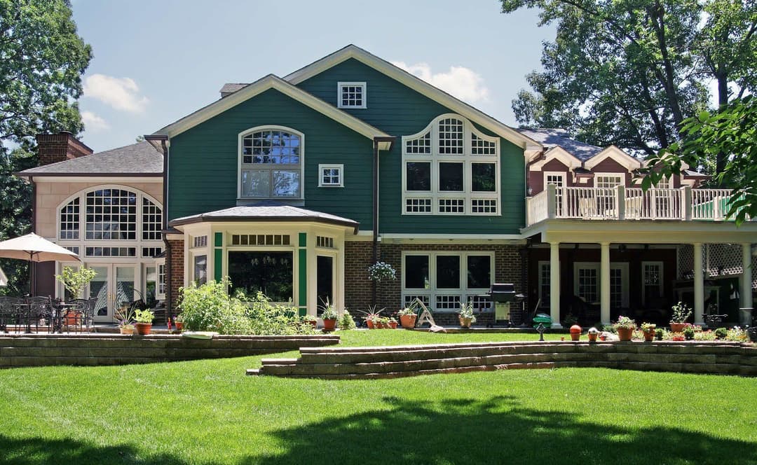 Elegant green and brick house with large windows and landscaped garden, perfect for outdoor living.