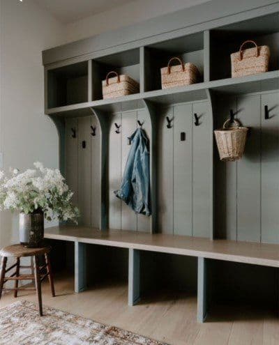 Stylish mudroom with green storage, baskets, hooks, and floral arrangement on a stool.