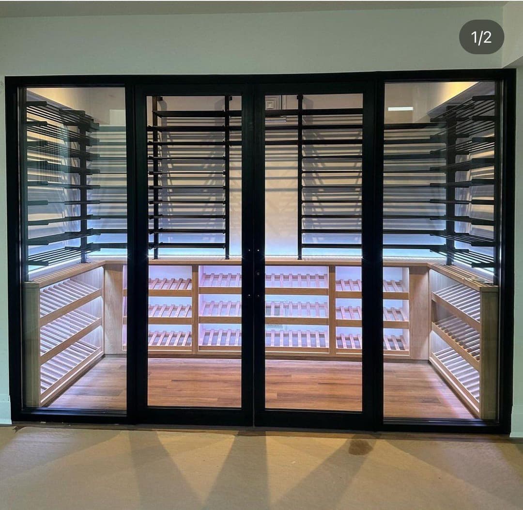 Modern wine cellar with wooden shelves and glass doors, featuring sleek black window frames.