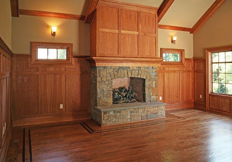 Cozy living room with a stone fireplace, wooden paneling, and large windows.