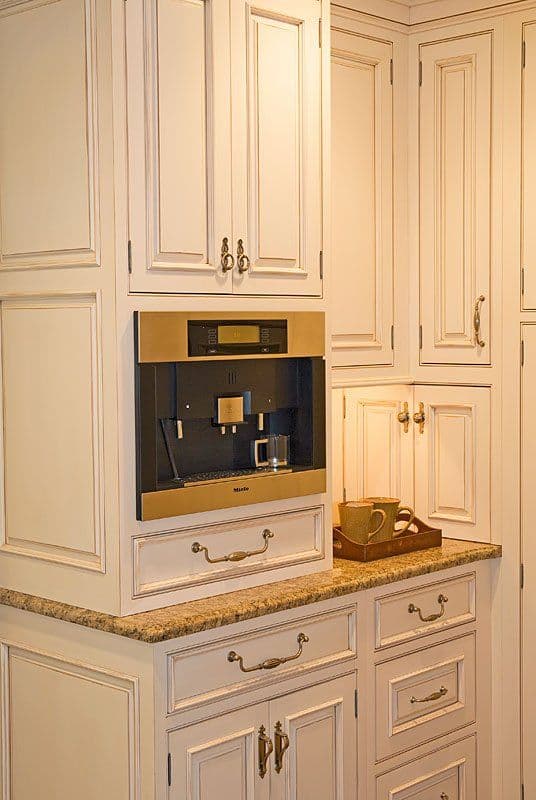 Modern kitchen featuring elegant white cabinetry and built-in coffee machine with granite countertop.
