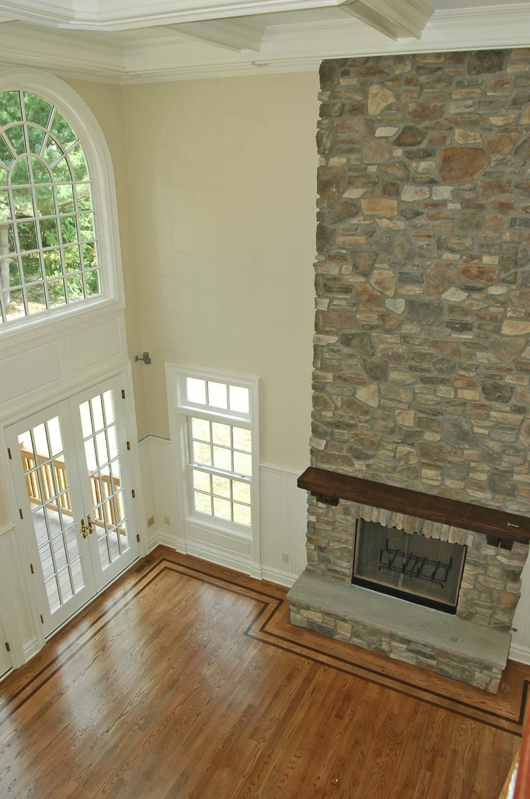 Spacious living room with stone fireplace, large windows, and hardwood floors.