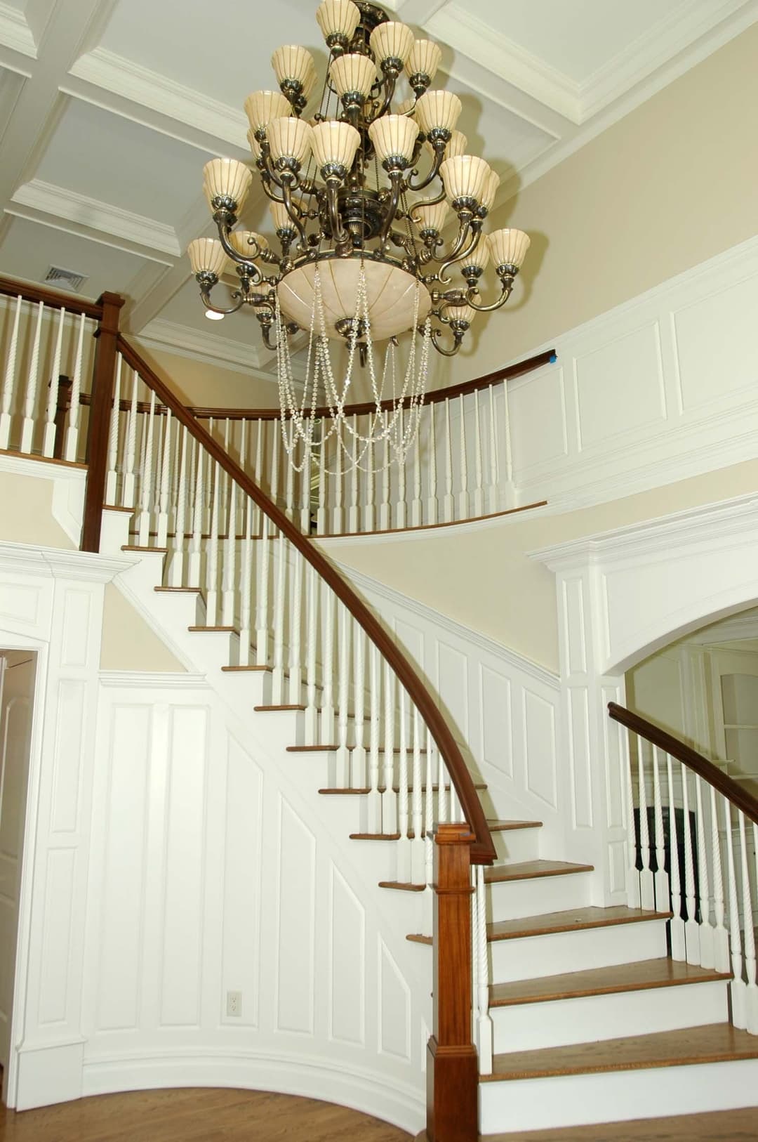 Elegant staircase with wooden railings and a luxurious chandelier in a bright entryway.