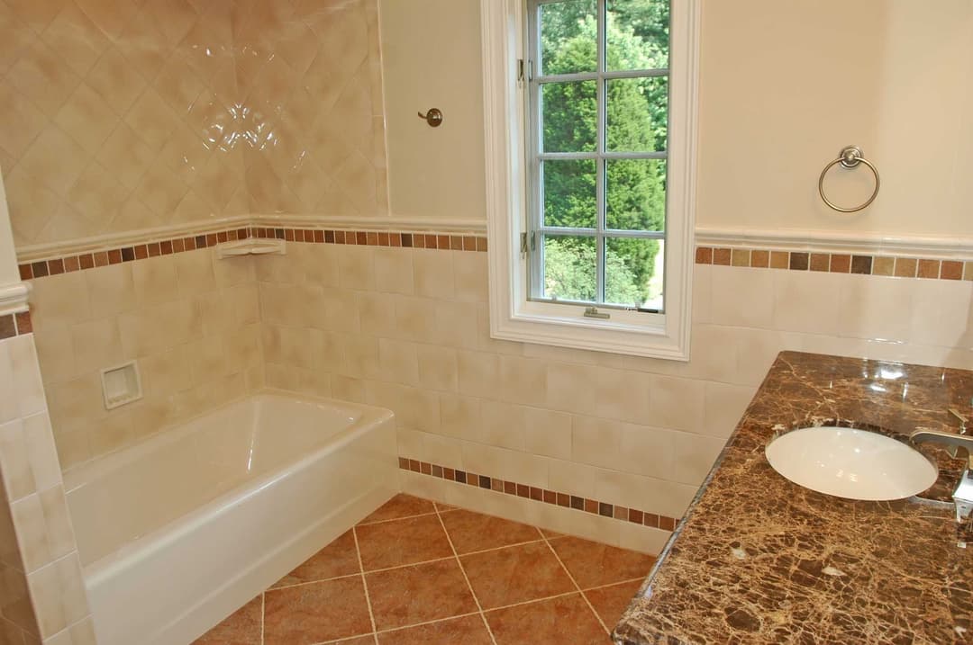Modern bathroom featuring a bathtub, marble countertop, and window with garden view.