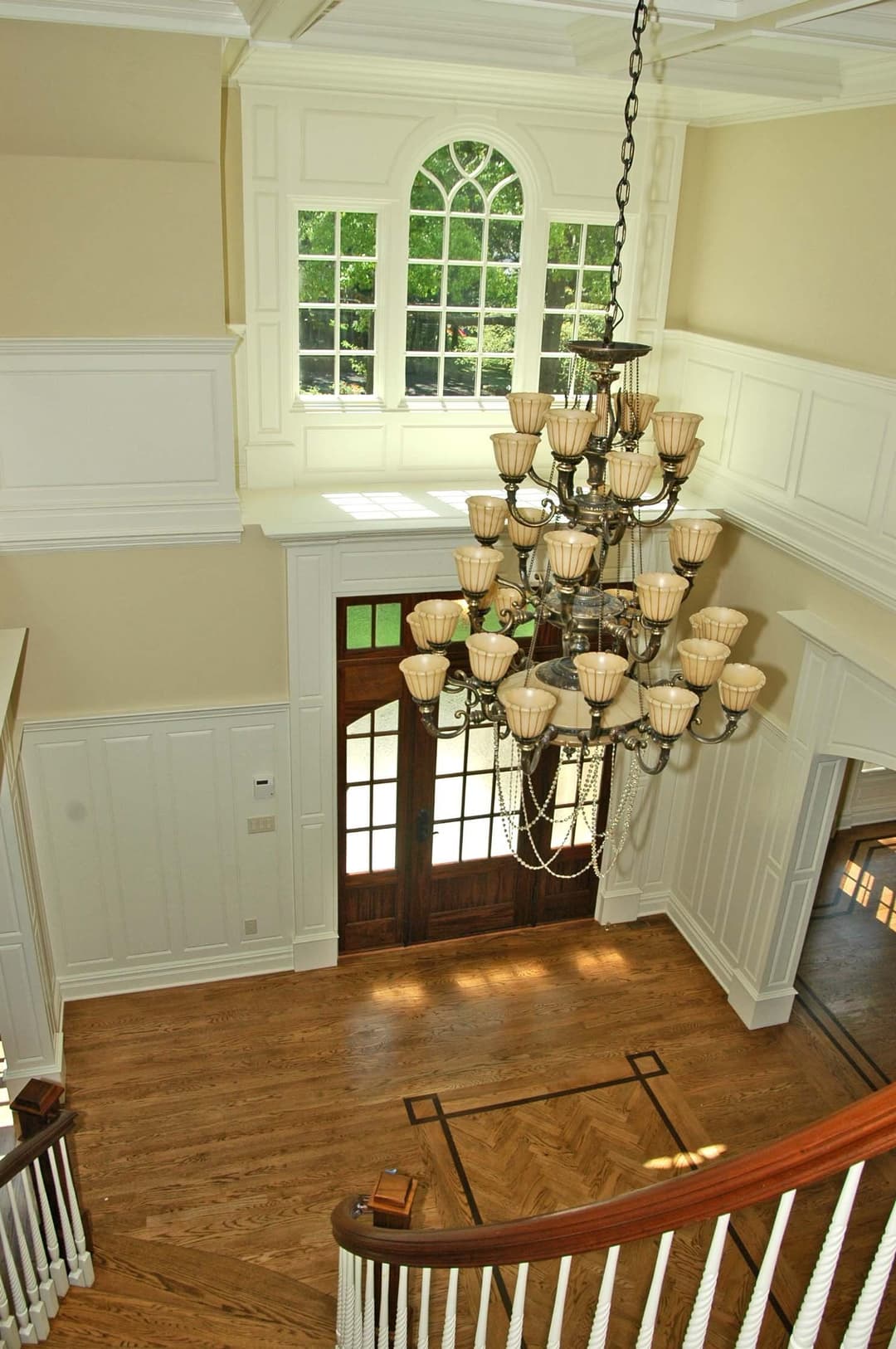 Elegant foyer with large chandelier, wooden staircase, and bright windows showcasing natural light.