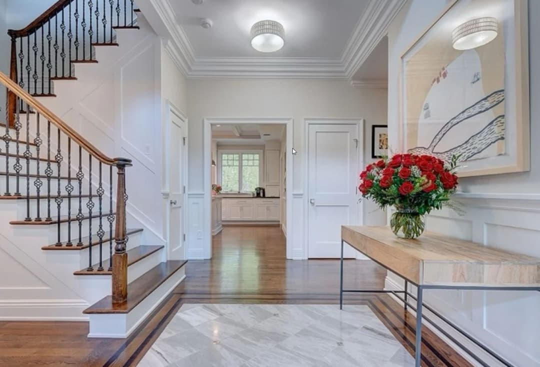 Elegant foyer with staircase, flowers, and open kitchen view in a stylish home interior.