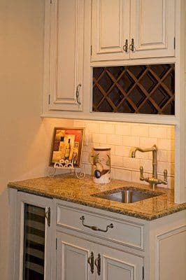 Elegant kitchen wet bar with granite countertop, under-cabinet lighting, and wine storage.