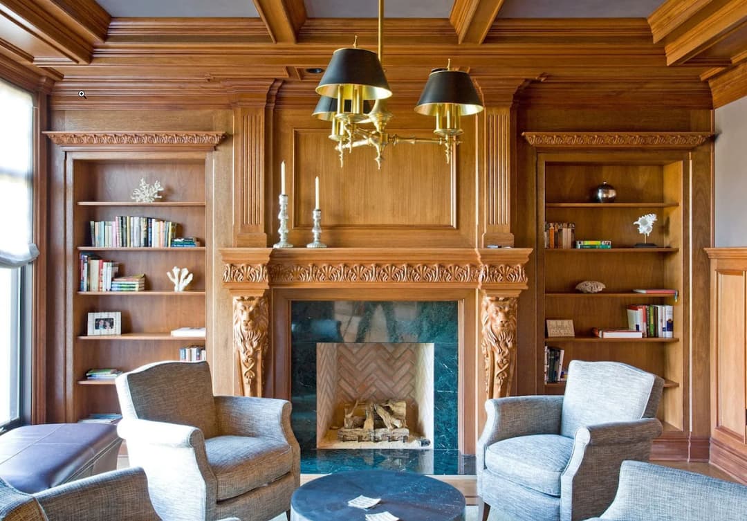 Elegant wood-paneled living room with a classic fireplace, two armchairs, and built-in bookshelves.