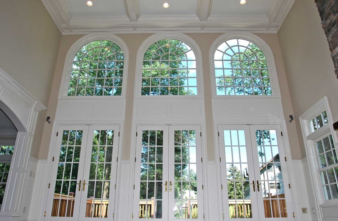 Elegant arched windows and double doors with natural light and greenery view.