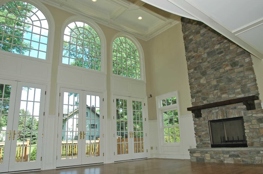 Spacious living room with large arched windows and a stone fireplace, bright natural light.