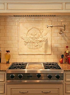 Elegant kitchen with a decorative fruit basket relief above a stainless steel gas range.