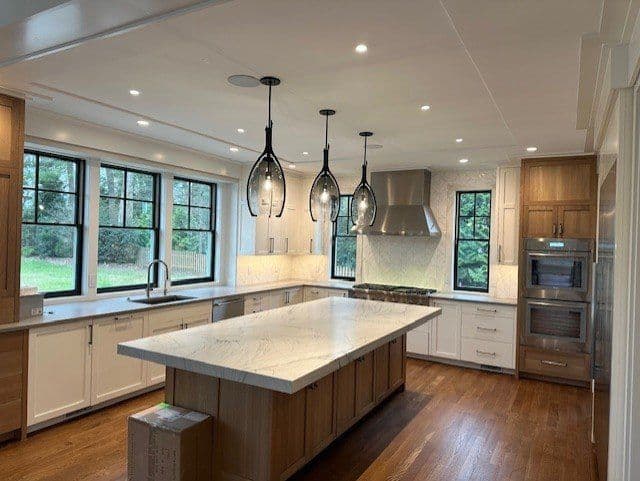 Modern kitchen featuring marble island, pendant lights, and stainless steel appliances.