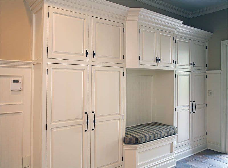 Elegant white built-in cabinetry with storage and a cushioned bench in a modern entryway.