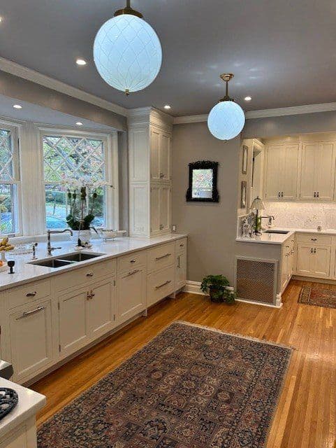 Modern kitchen with white cabinetry, pendant lights, hardwood floor, and elegant decor.