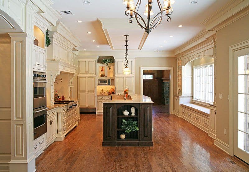 Stylish open kitchen with white cabinetry, dark island, hardwood floors, and elegant lighting.