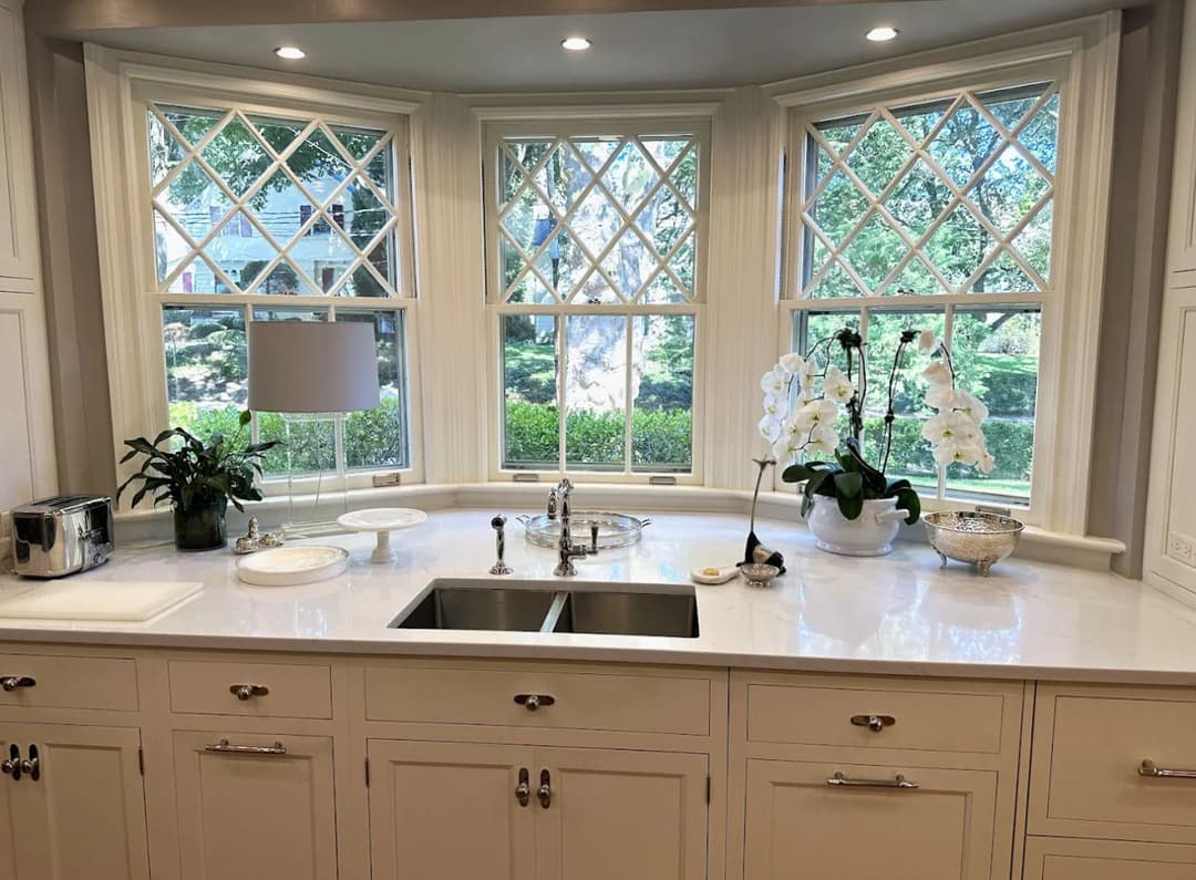 Bright kitchen with large diamond-pane windows, elegant white cabinetry, and modern fixtures.