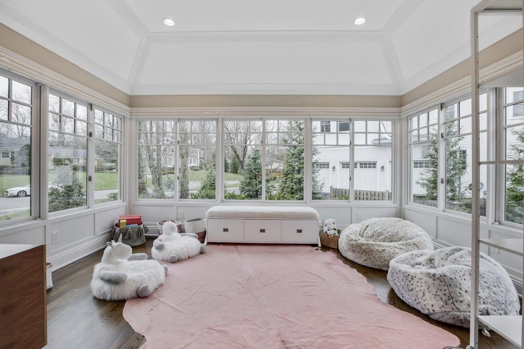 Bright sunroom with large windows, cozy bean bags, and a soft pink rug, ideal for relaxation.