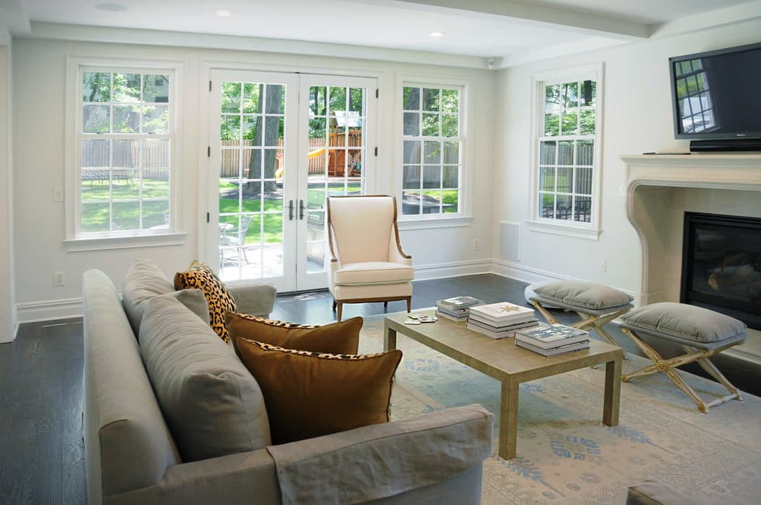 Modern living room with a cozy sofa, armchair, and large windows overlooking a garden.
