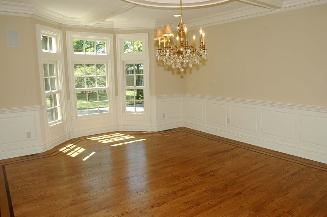 Spacious empty room with hardwood floors, large windows, and a chandelier. Perfect for staging.