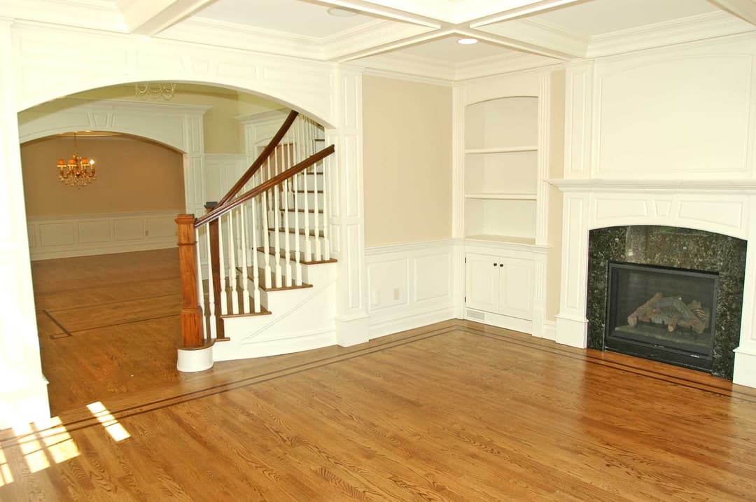 Spacious living room with hardwood floors, fireplace, and elegant staircase. Natural light highlights design.