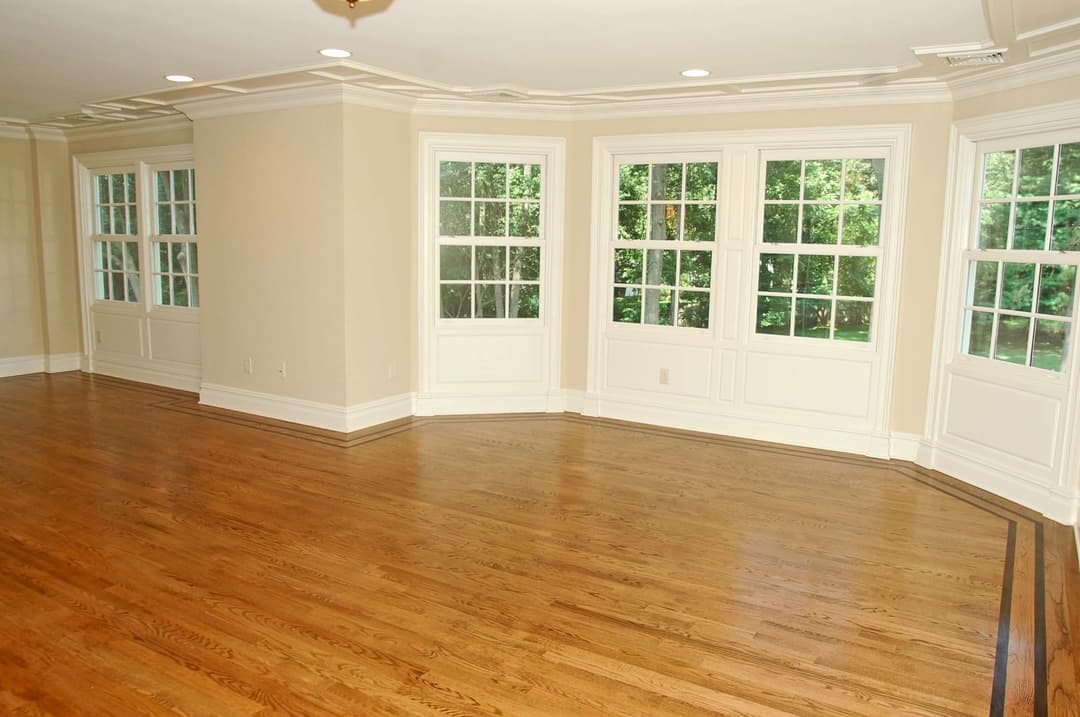 Spacious empty room with hardwood floors and large windows overlooking a green landscape.