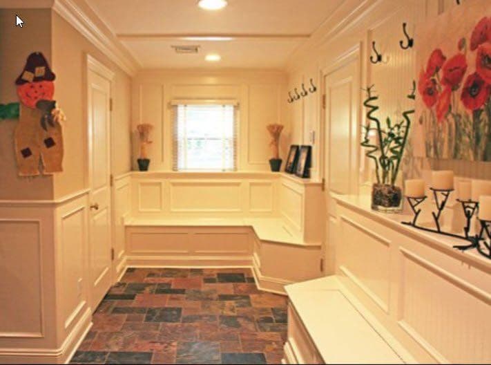 Bright entryway with slate flooring, wall hooks, and floral artwork, featuring a cozy seating area.