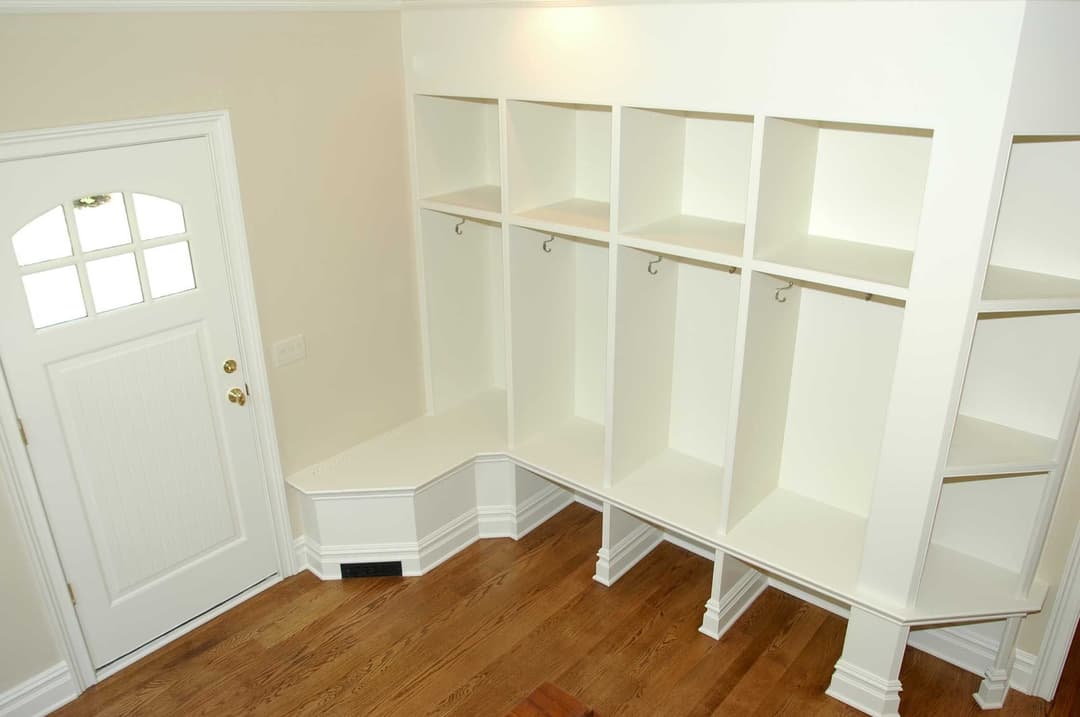 Modern mudroom benches and hooks with white cabinetry and wooden flooring. Cozy entryway design.